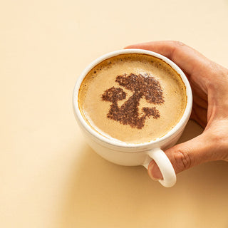 A hand holding a cup of coffee with a tree design in the foam.