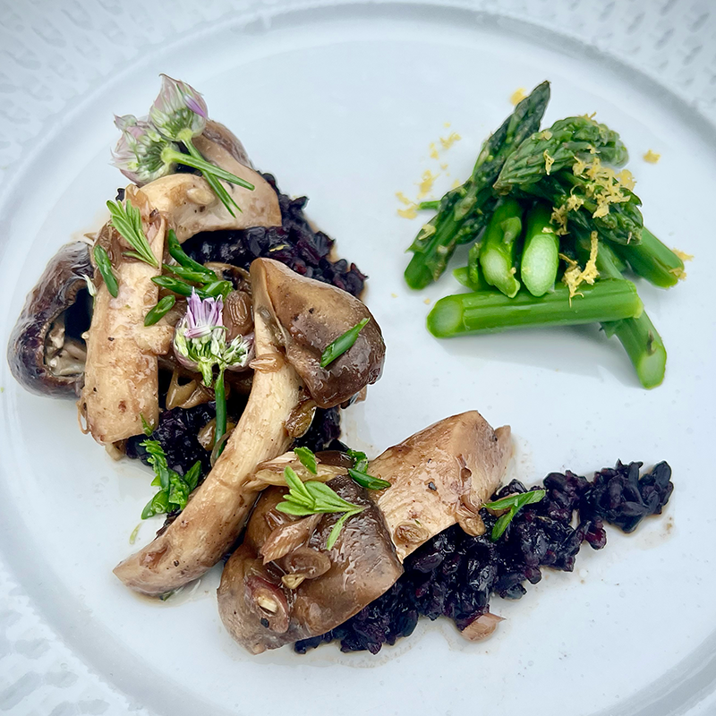 A plate of black rice with mushrooms and green vegetables.