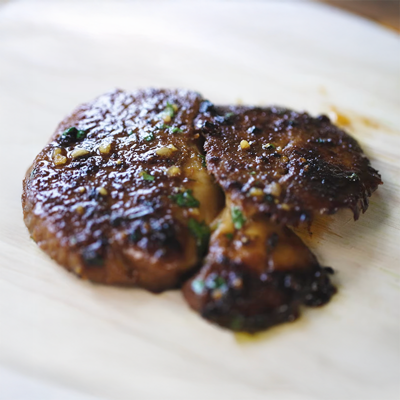 Cooked meat with a caramelized surface and herbs on a wooden plate.