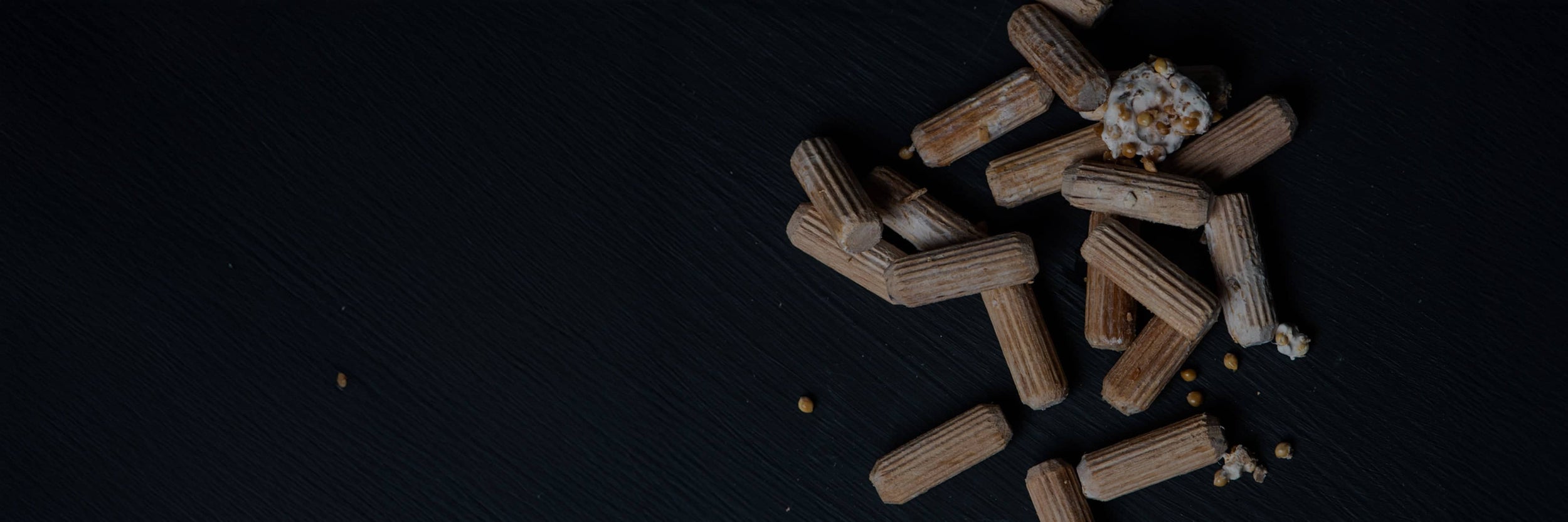 Scattered pieces of brown, rectangular cereal and a few popcorn kernels on a dark, textured surface.