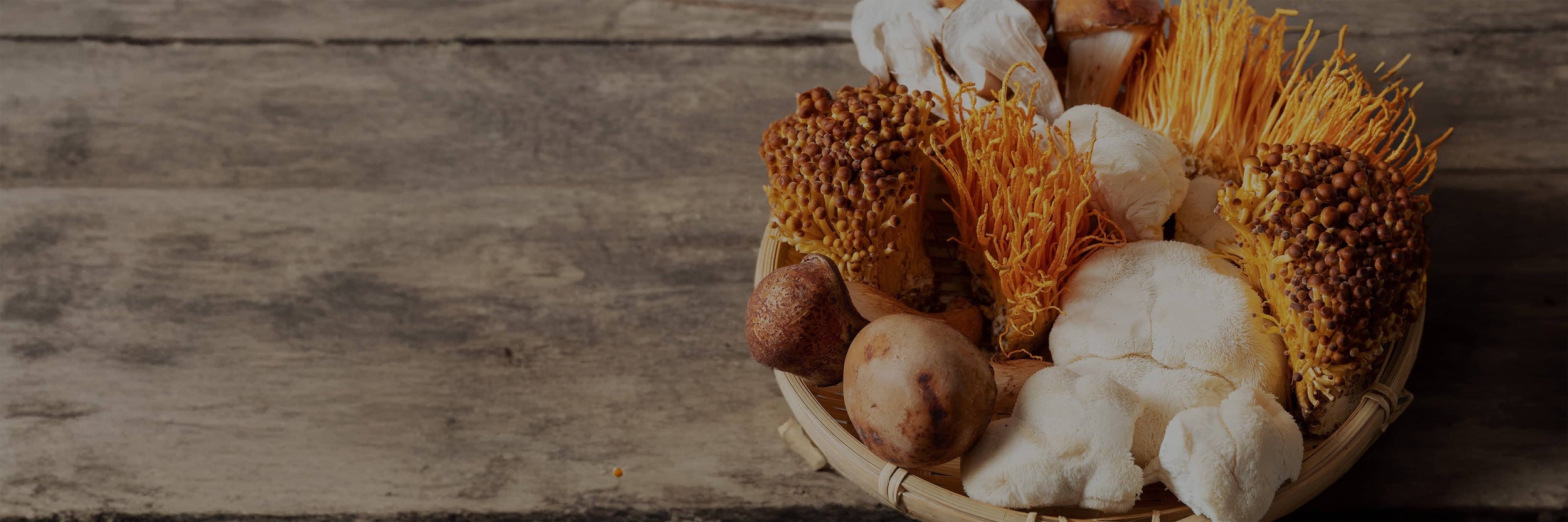 A woven basket filled with assorted mushrooms including orange, white, and brown varieties, placed on a rustic wooden surface.