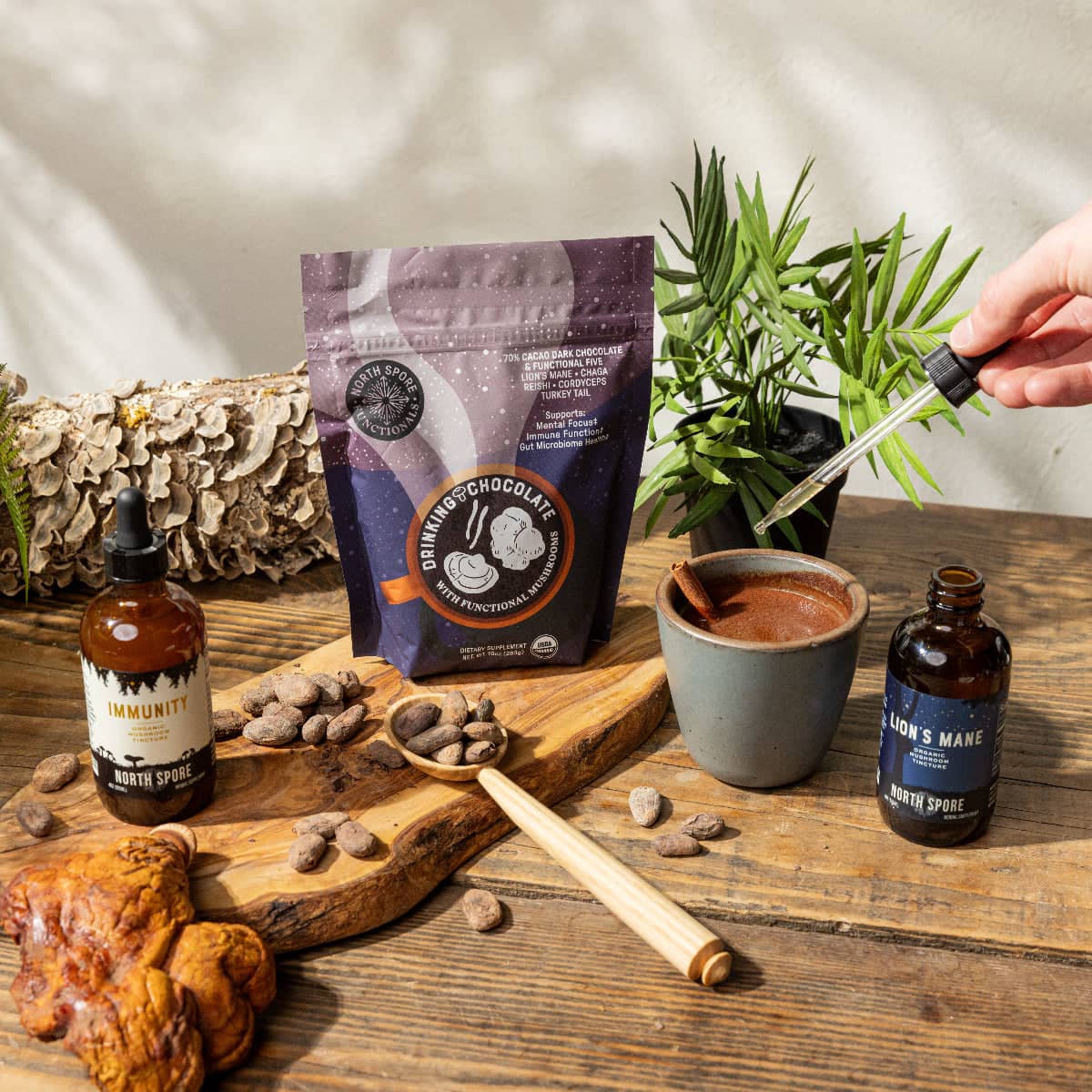 Table with natural products including a bag of drinking chocolate, a bottle of 'Immunity North Spore', and a cup of hot chocolate.