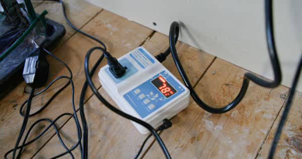 A digital temperature controller plugged in on a wooden floor displays 78.8°F, with several cables connected to it and running nearby.