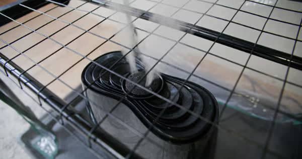 A black humidifier emits a visible stream of mist upward through a metal grid or wire shelf above it.