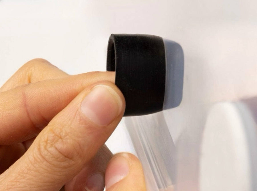 A close-up of a hand holding a black silicone ring or grommet against a translucent white plastic surface.