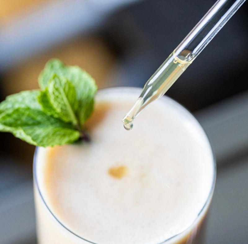 A close-up shows a creamy drink with mint as a North Spore Mind & Body Mushroom Tincture Variety Pack (Small) is dropped in above the surface.