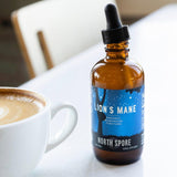 Image thumbnail: A brown glass dropper bottle of North Spore’s Mind & Body Mushroom Tincture Variety Pack (Small) sits next to a cup of coffee on a white table.